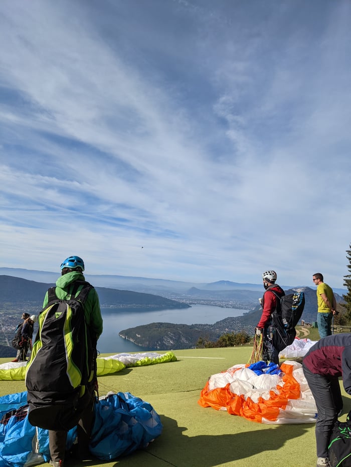 Services Adventure-seekers gear up for paragliding with panoramic views of a vast lake and lush hills under a bright sky.