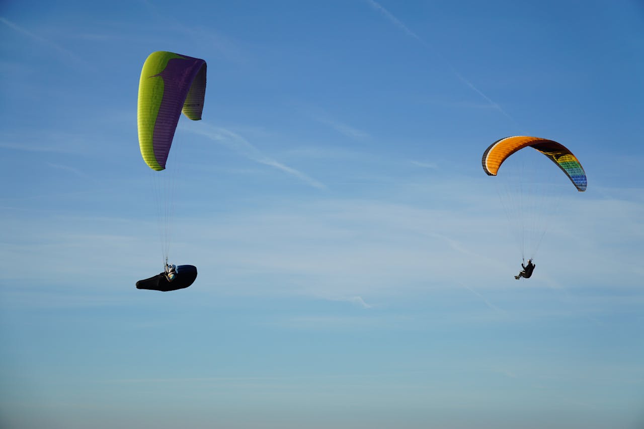 About Two colorful paragliders soar gracefully against a clear blue sky in Millau, France.