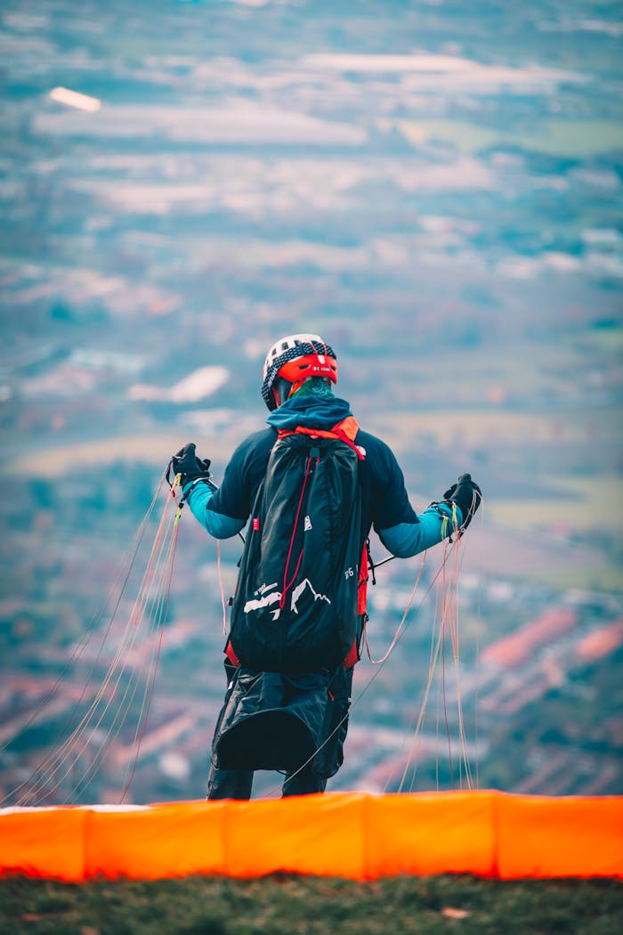 Paraglider in gear ready to take off on a scenic hillside with colorful canopy.