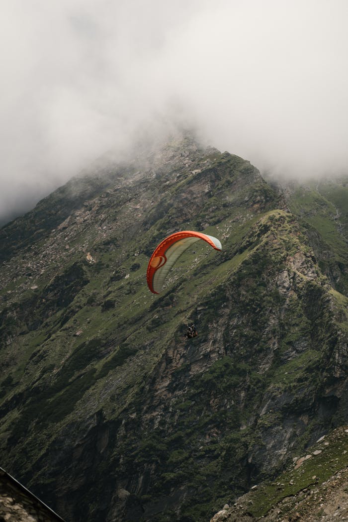 Services Experience the thrill of paragliding with breathtaking views of rugged mountain terrain beneath cloudy skies.